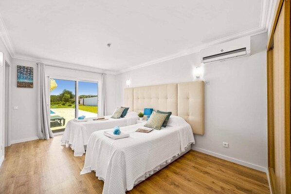 A hotel room with two beds, a large window, and an air conditioning unit.