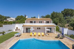 A two-story house with a swimming pool and multiple lounge chairs.