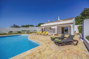Un espace aménagé au bord de la piscine, avec des chaises longues, une piscine et un bâtiment doté d’un toit en tuiles.