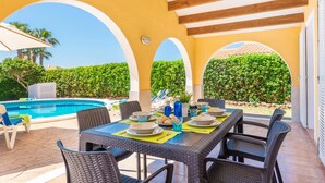 A covered outdoor dining area with a pool, wicker furniture, and a clear view of the sky. - Villa Pluton by Villa Plus (Cap d'Artrutx)