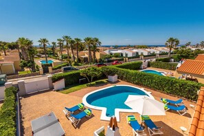A resort with a central swimming pool, lounge chairs, and palm trees. - Villa Pluton by Villa Plus (Cap d'Artrutx)