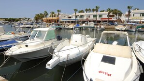 A marina with several boats docked, a café, and palm trees in the background. - Villa Pluton by Villa Plus (Cap d'Artrutx)