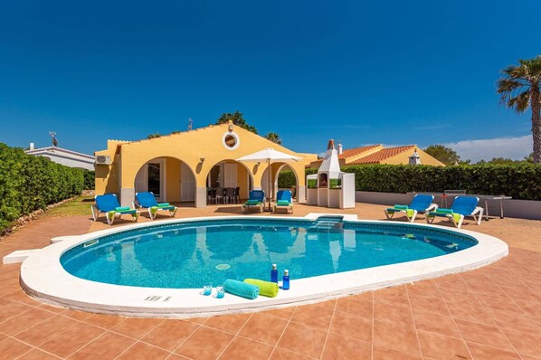 A swimming pool with lounge chairs, a covered seating area, and a building with arches.