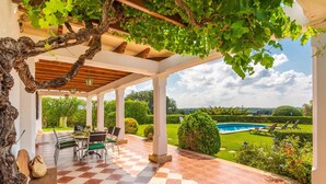 Un portico coperto con pavimento a scacchi, mobili da esterno e vista su piscina e giardino.