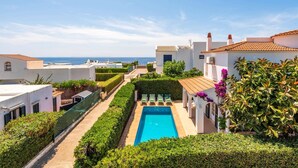 Ein Poolbereich mit freiem Blick auf das Meer, umgeben von weißen Gebäuden mit Terrakotta-Dächern und einem gepflegten Heckenstreifen am Poolrand.