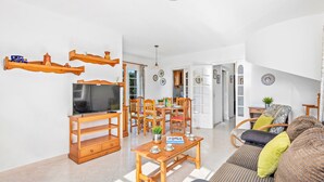 Ein großzügiger Wohnbereich mit einem Holz-Fernsehmöbel, einem Esstisch mit Stühlen, einem Sofa und einem Bücherregal.
