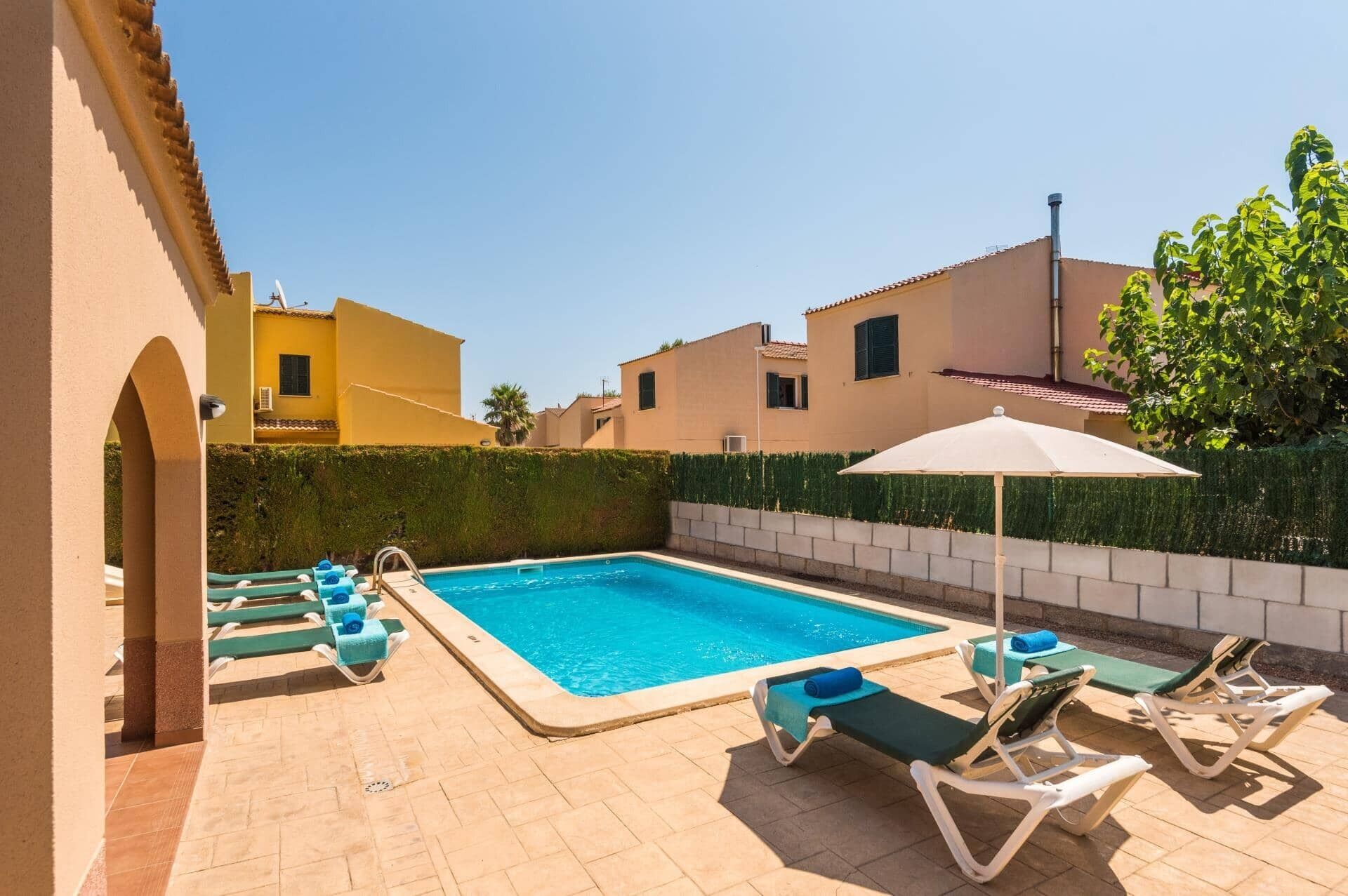 Ein Pool mit Liegestühlen und Sonnenschirmen, umgeben von einer niedrigen Hecke und Gebäuden.