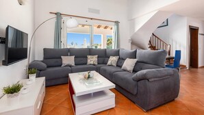 A living room with a grey sofa, a white coffee table, a TV mounted on the wall, and a staircase leading to an upper level.