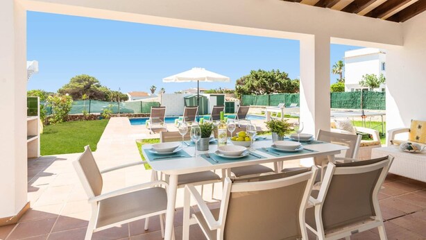 An outdoor patio with a pool, dining table, chairs, and umbrellas.