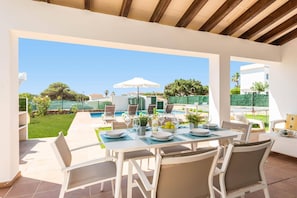 Eine Terrasse im Freien mit Pool, Esstisch, Stühlen und Sonnenschirmen.