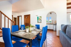 A dining area with a table set for four, blue chairs, a kitchen in the background, and a staircase leading to another level.