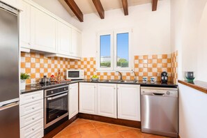 A kitchen with white cabinets, a microwave, a stove, a dishwasher, and a window with a view.