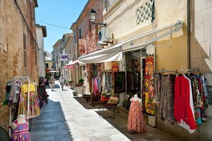 A narrow street with shops on either side, displaying various clothing items.