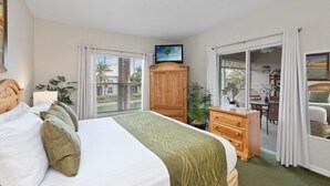 A hotel room with a bed, a wooden dresser, a television on a stand, and a balcony with a view of the outside. - Lely Greenlinks 2nd Floor - on Golf Course, Minutes from Beaches, Downtown! (Naples)