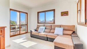 A spacious living room with a large sofa, two windows with a view, and a small table.