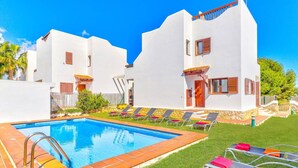 A pool area with a clear blue pool, surrounded by white buildings with balconies and wooden shutters.
