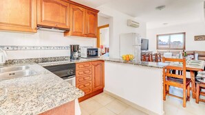 A kitchen with wooden cabinets, granite countertops, a coffee maker, a microwave, and a refrigerator.