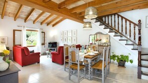 A spacious living area with a dining table set for four, a red sofa, and a staircase leading to an upper floor. - Villa Mari Pollensa by Villa Plus (Mallorca)