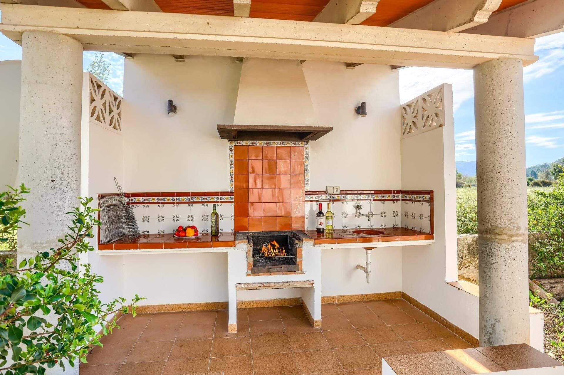 An outdoor kitchen with a grill, tiled backsplash, and a view of the surrounding landscape.