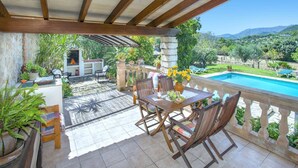 A covered patio with a pool, wooden furniture, and potted plants.