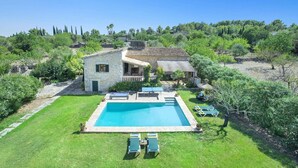 A stone house with a swimming pool, surrounded by lush greenery and trees.
