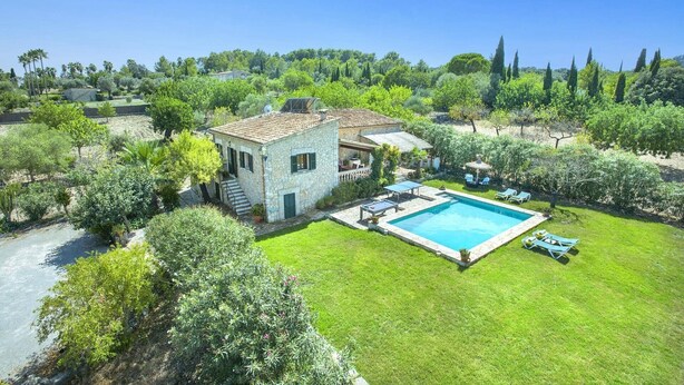 A stone house with a swimming pool, surrounded by lush greenery and trees.