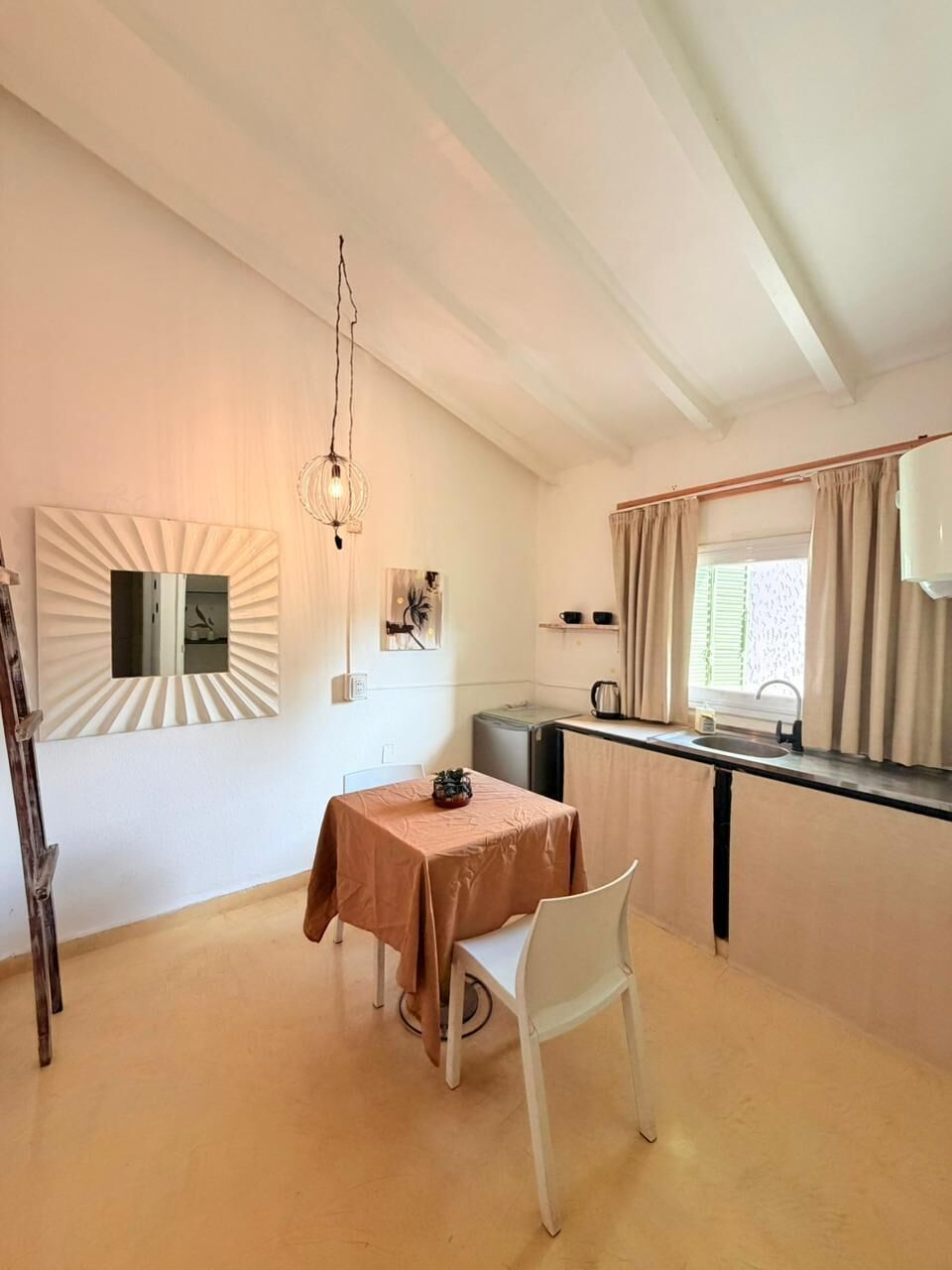 Uma cozinha compacta com área de jantar, luminária pendente e janela com cortinas.