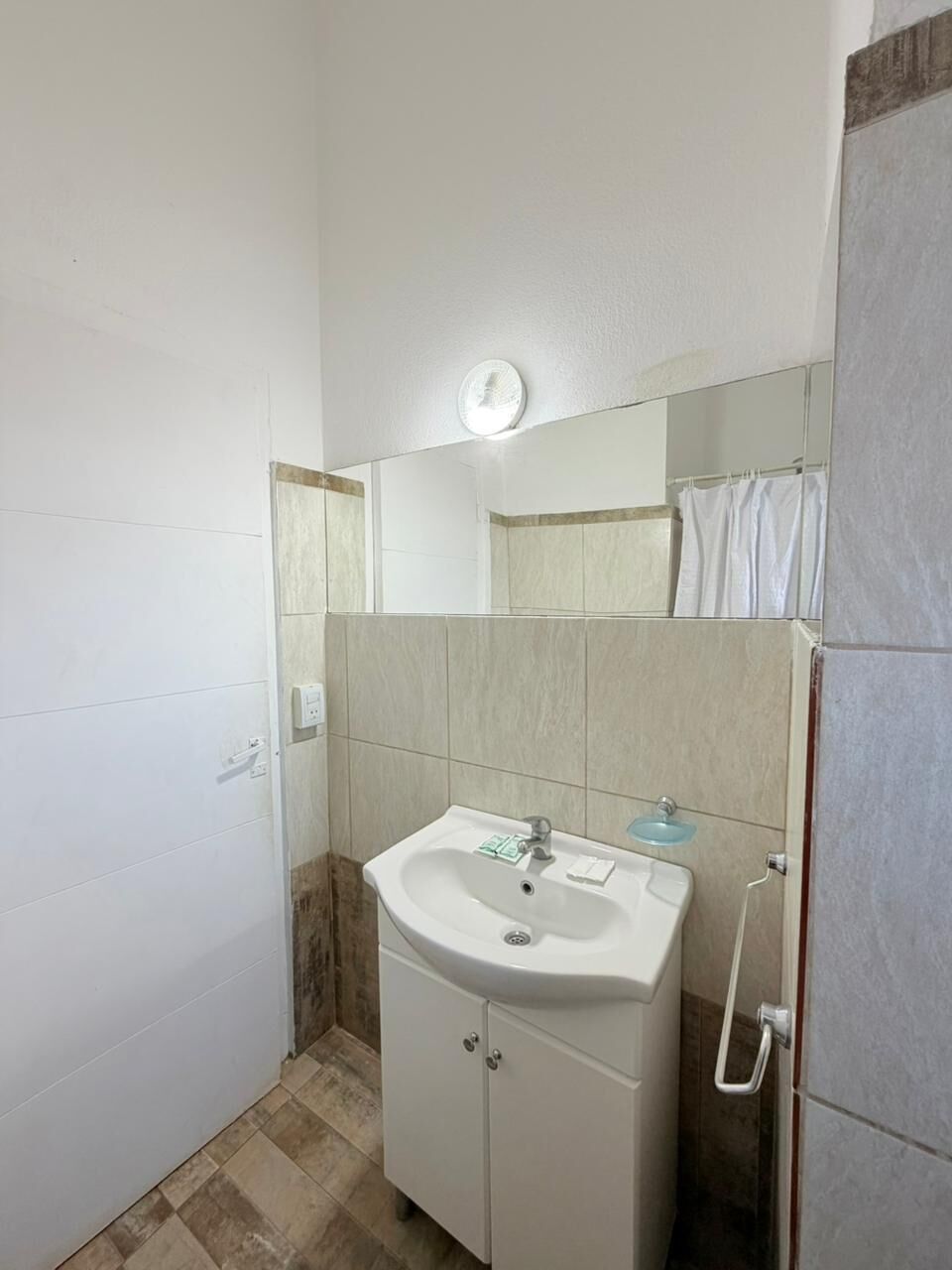 A small bathroom with a white sink, a mirror, and a shower area.