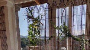 Taula amb un pastís, un bocal de melmelada, una teiera i un got d'aigua, amb vistes a la vegetació i un edifici al fons.
