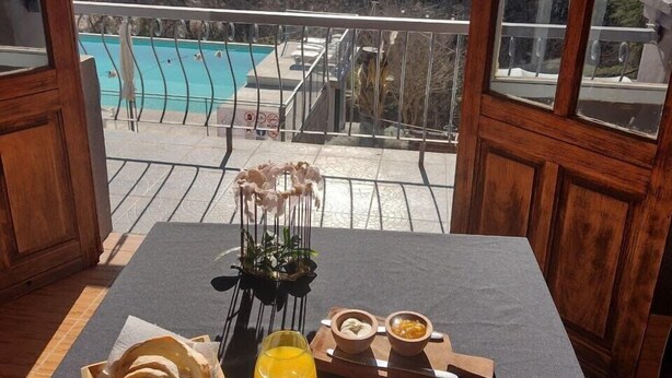 Taula de desballestament amb pa, suc d'aranja, cafè i pastissos, amb vista a una piscina i muntanyes.