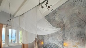 Un dormitori amb un llit amb cortina, un finestral gran i una paret amb un dibuix de fulles.