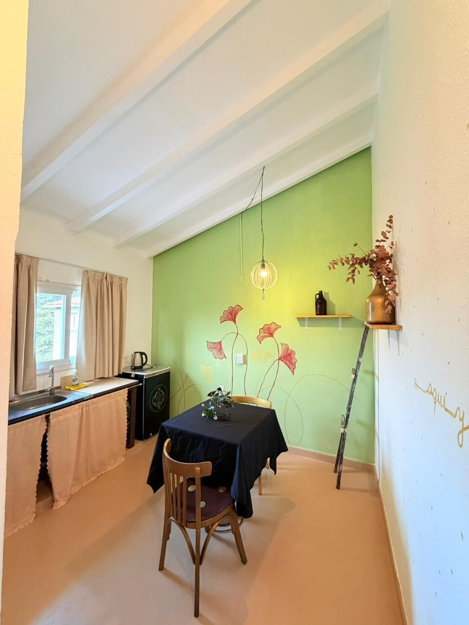 A dining area with a table, chairs, a hanging light fixture, a window with curtains, and a green wall.