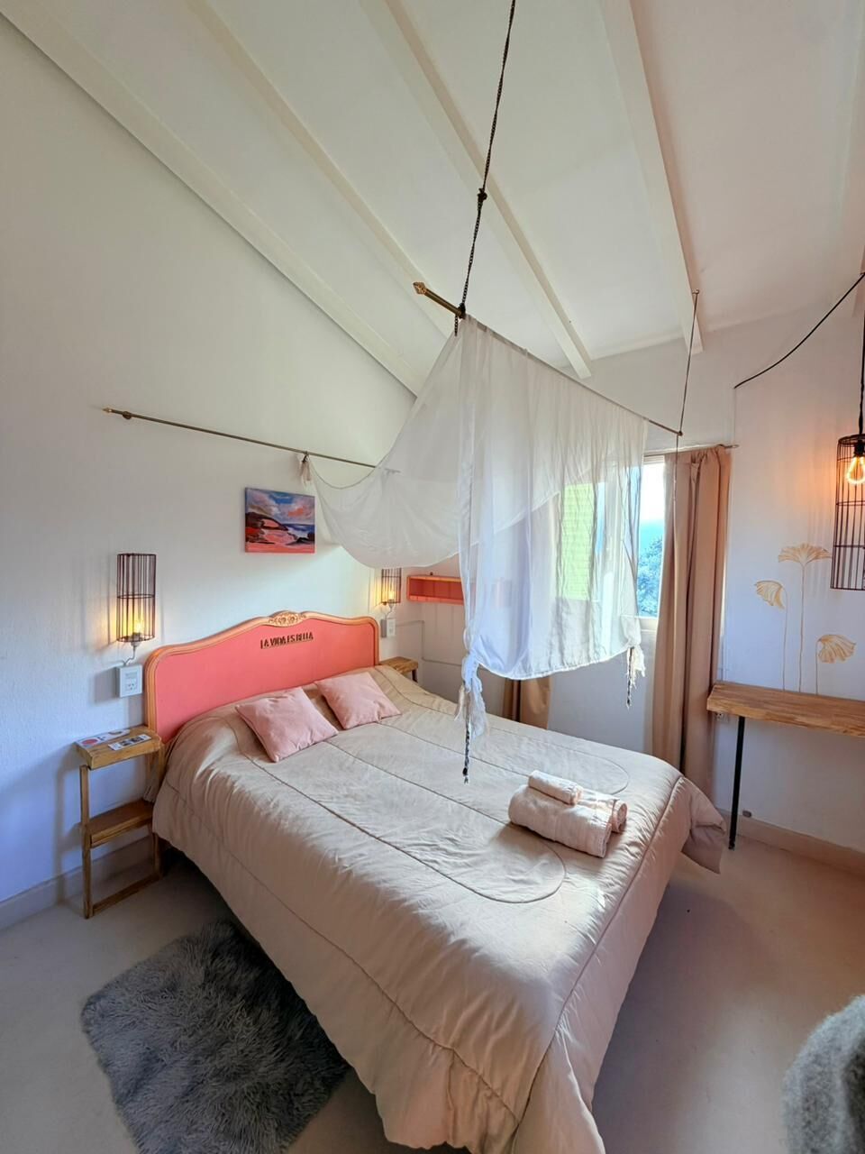 Un dormitorio con cama, dosel, mesita de noche, lámpara y un cuadro en la pared.