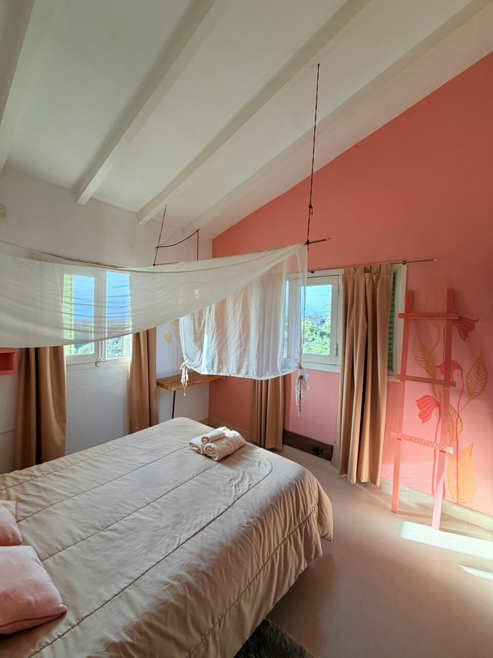 Un dormitorio con cama, cortinas, ventana y una pared decorada con motivos florales.