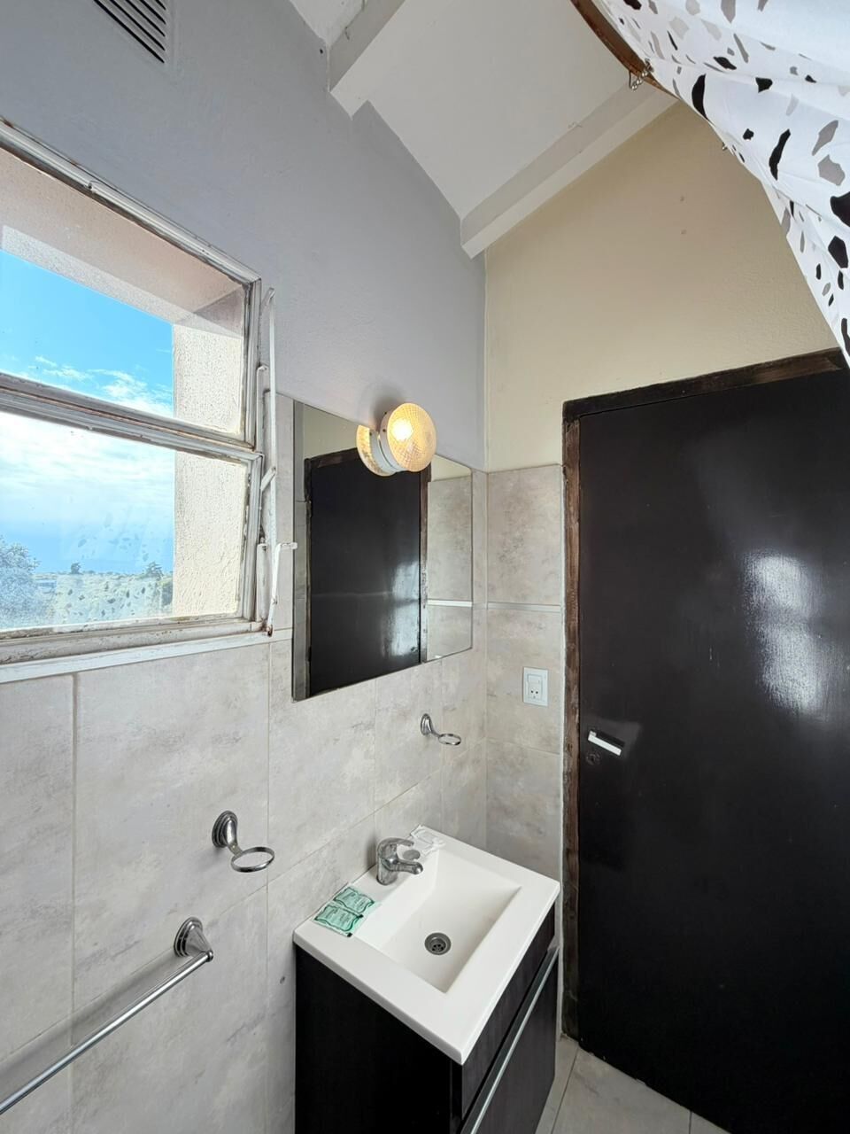A bathroom with a window, a sink, a mirror, and a door.