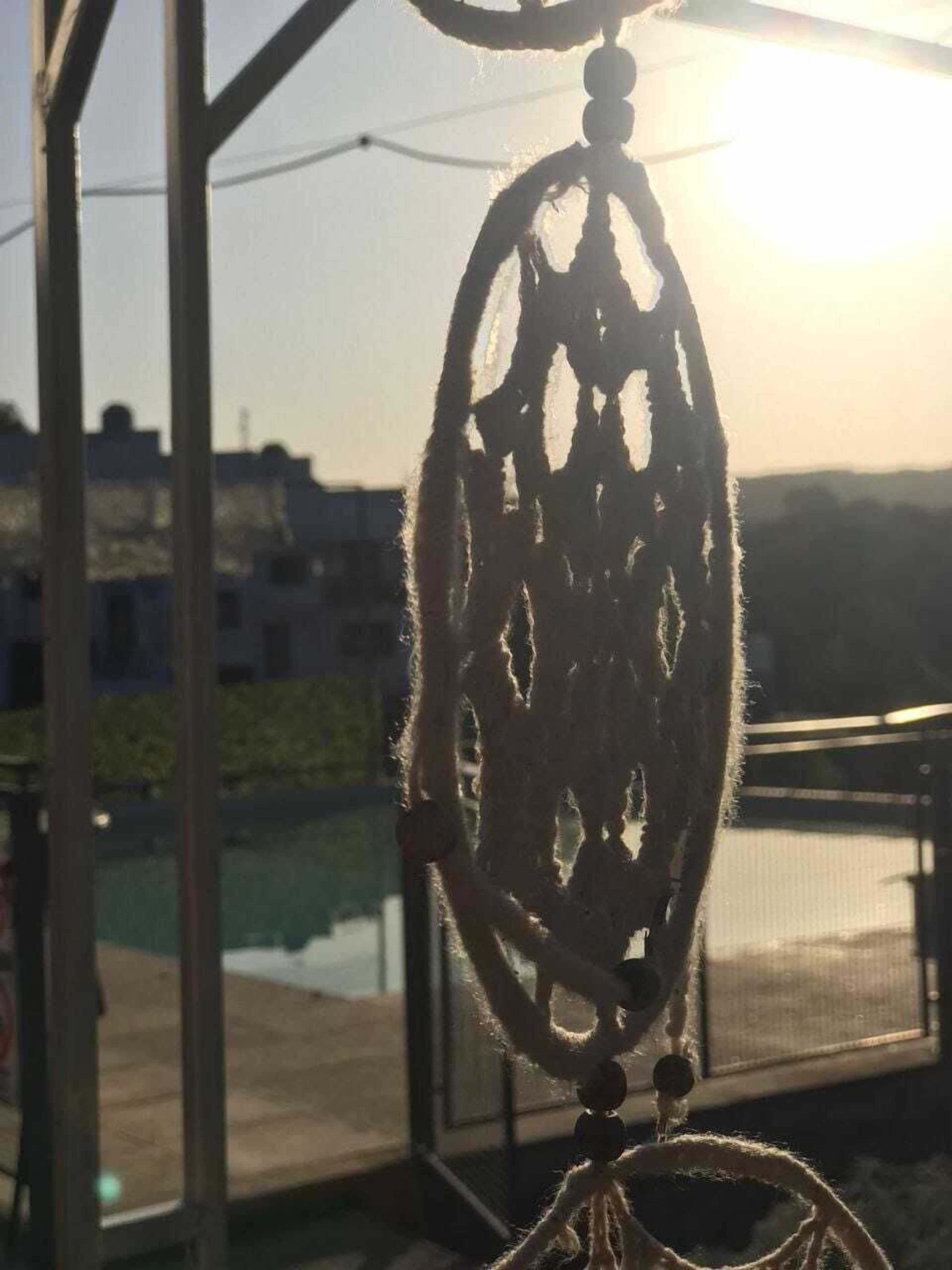 A dreamcatcher hanging in a room with a view of a cityscape and a body of water.