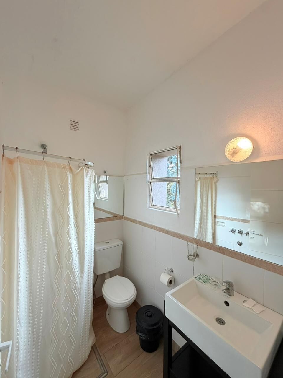 A bathroom with a shower curtain, toilet, sink, and a window.