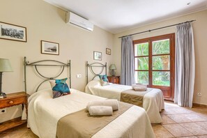 Une chambre d’hôtel avec deux lits, une fenêtre avec des rideaux, une table de chevet avec une lampe et un climatiseur fixé au mur.
