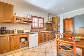 Une cuisine avec des meubles de rangement en bois, une machine à café, un grille-pain et une table à manger avec des chaises.