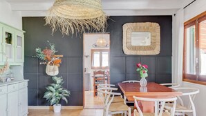 Un coin repas avec une table en bois et des chaises blanches, une plante en pot et une décoration murale tissée.