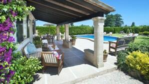 A covered outdoor patio with seating, a pool, and lush greenery.