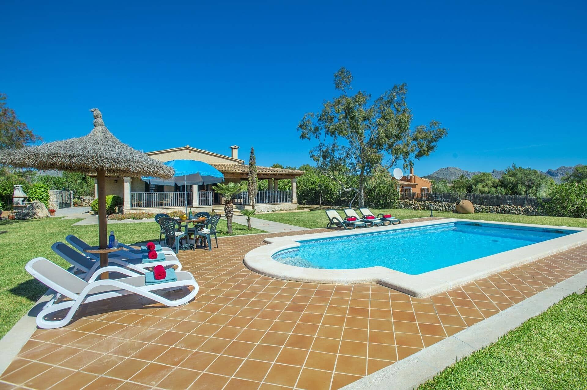 A swimming pool with lounge chairs, a thatched umbrella, and a house with a tiled patio.