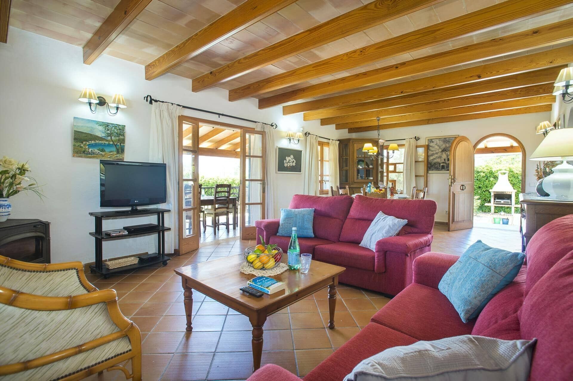 A spacious living room with a red sofa, wooden ceiling beams, and a television.