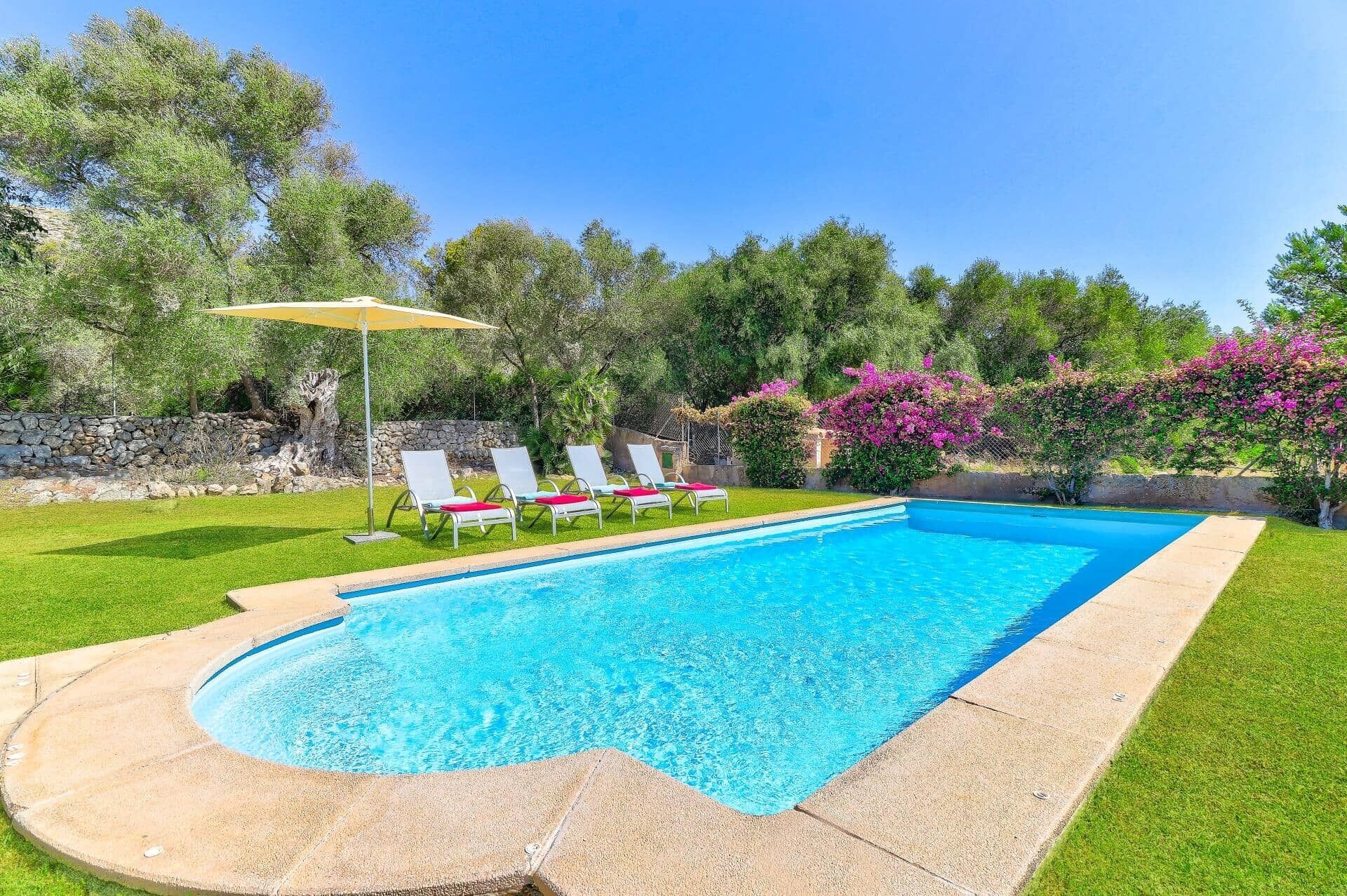 Une piscine bordée de pierres, entourée d’une pelouse bien entretenue et d’un mur de pierres.