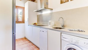 A compact kitchen with white cabinets, a stainless steel sink, a built-in range hood, and a dishwasher. - Villa Olivo by Villa Plus (Mallorca)