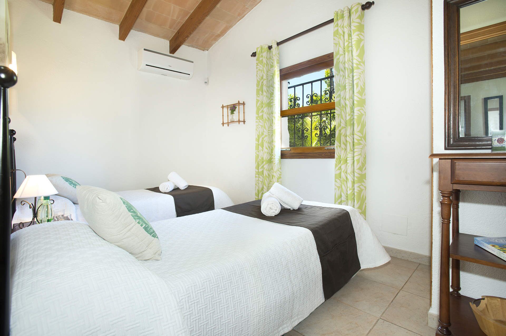 A hotel room with two beds, a window with a view, a wooden desk, and an air conditioning unit.