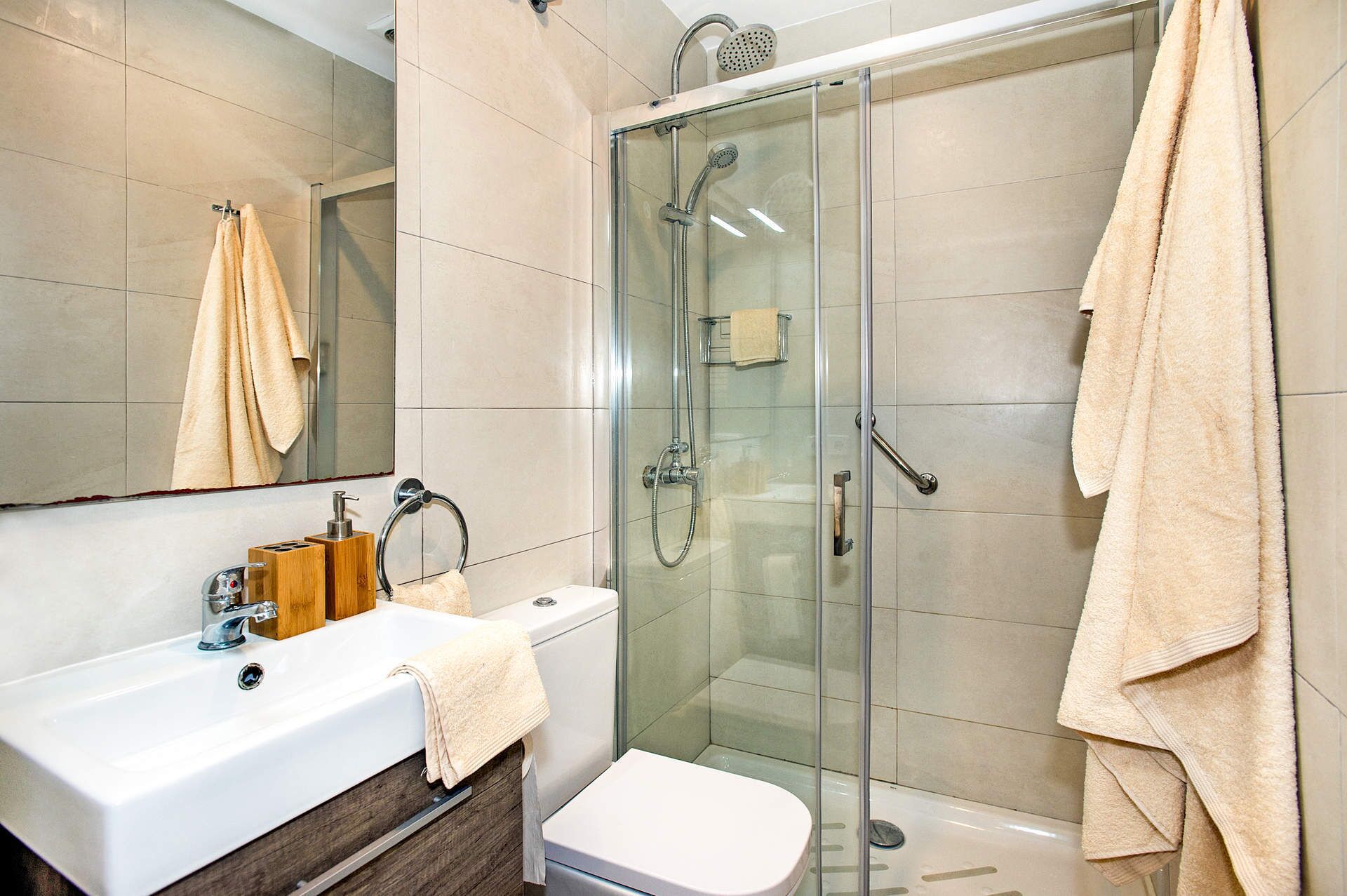 Un bagno moderno con cabina doccia in vetro, un lavandino bianco e un dispenser di sapone in legno, e un water.