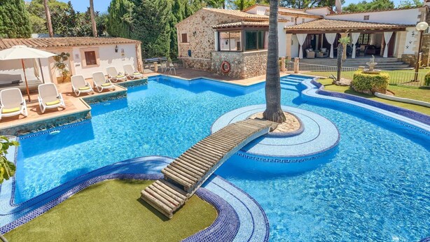 A swimming pool with a wooden slide, lounge chairs, and a stone building.