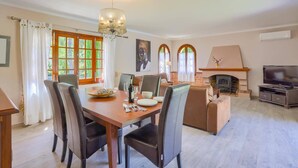 A dining area with a wooden table, chairs, a chandelier, and a fireplace.