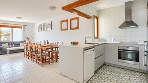 Una cucina moderna con mobili bianchi, lavastoviglie integrata e piano cottura. È presente una zona pranzo con sedie in legno e un tavolo, e opere d'arte alle pareti.